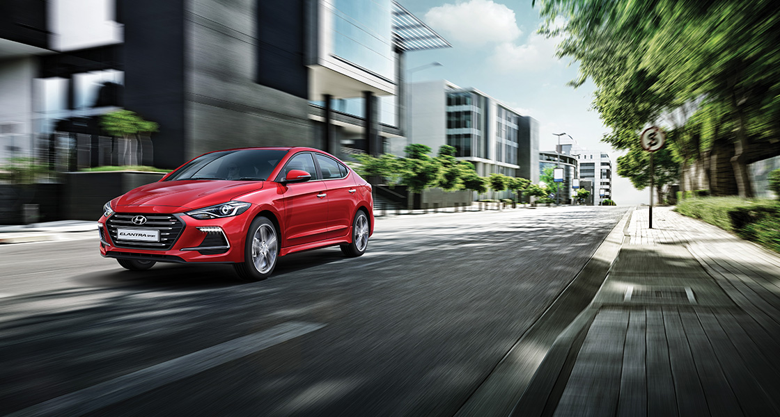 Left side front view of red Elantra Sport driving on the street