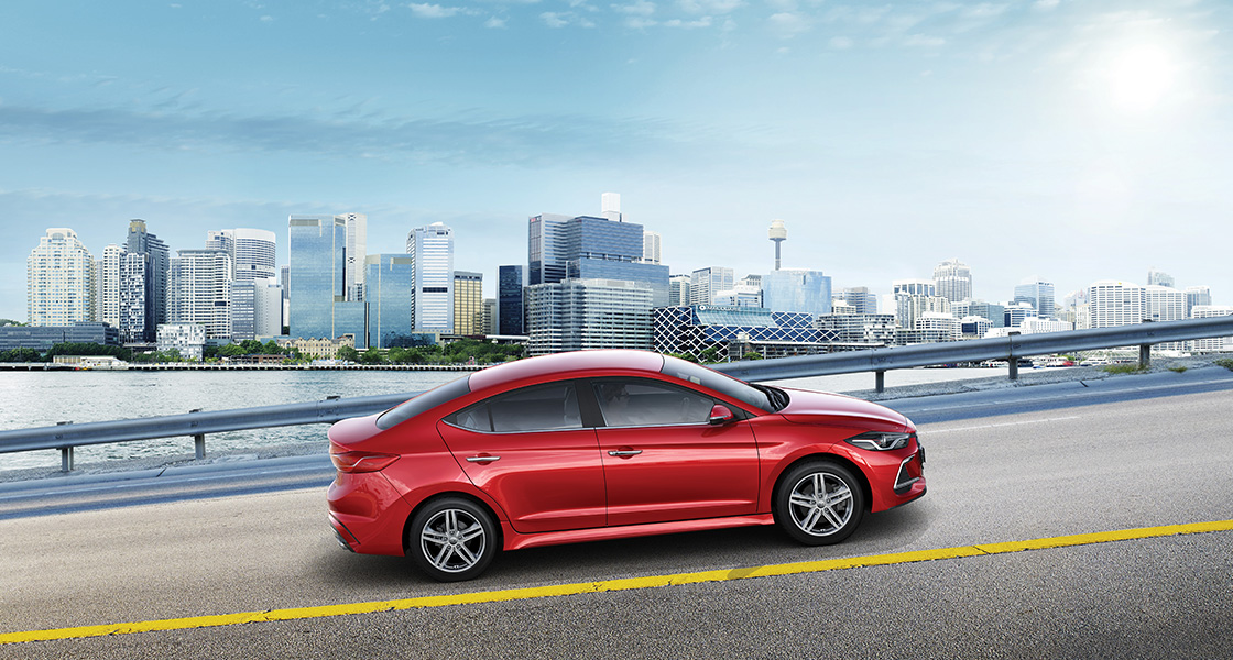 Side view of red Elantra Sport on the road with buildings background